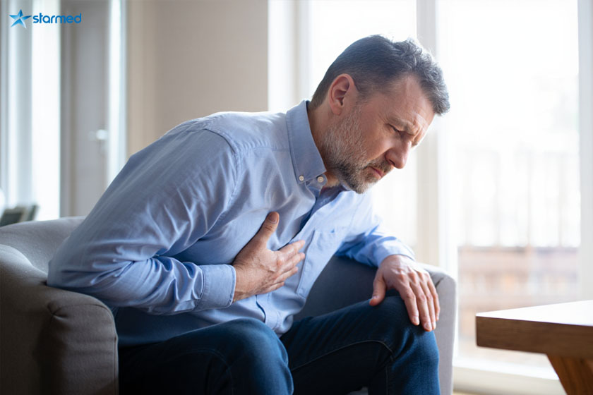 Мужчина сидит в кресле и держится рукой за сердце